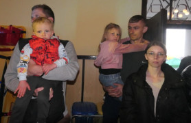 Dorośli i dzieci stoją obok siebie. Małe dzieci trzymane są na rękach 