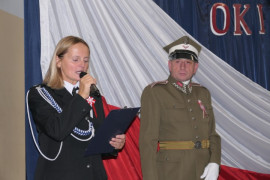 Kobieta i mężczyzna. Oboje w mundurach. Kobieta trzyma w ręku mikrofon 
