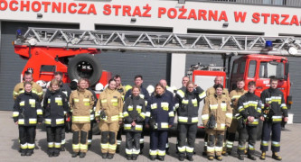 Grupa osób strażacy ochotnicy na wspólnej fotografii na tle bojowego wozu strażackiego 