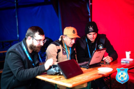 Trzej mężczyźni siedzą obok siebie. Przed nimi stoją laptopy 