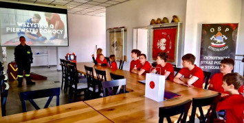Szkolenie MDP. Adepci sztuki pożarnictwa siedzą przy stole. Widoczny ekran i osoba prowadząca szkolenie 