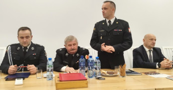 Czterej panowie w mundurach strażackich. Jeden z nich stoi i przemawia