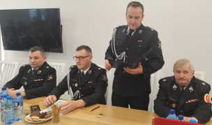 Czterej panowie w mundurach strażackich. Jeden z nich stoi i przemawia