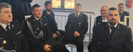 Grupa mężczyzn w mundurach strażackich. Mężczyźni siedzą obok siebie na krzesłach