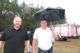 Dwaj mężczyźni stoją obok siebie. Jedne z nich trzyma parasol 