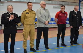 Pięciu mężczyzn stoi obok siebie. Jeden z nich trzyma w ręku mikrofon 