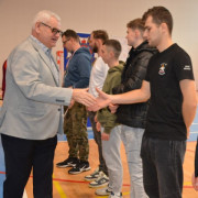 Mężczyźni stoją w szeregu obok siebie. Dwóch z nich podaje sobie ręce 