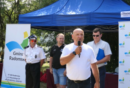 Grupa osób. Mężczyzna przemawia trzymając w ręku mikrofon