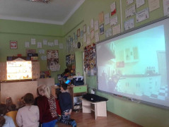 Dzieci siedzą na dywanie i oglądają film przygotowany przez strażaków 