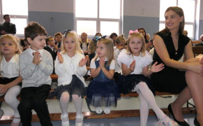 Dzieci siedzą na ławce. Obok dzieci siedzi kobieta 