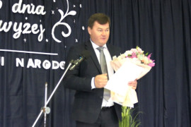 Mężczyzna stoi przy mikrofonie i przemawia. Mężczyzna w ręku trzyma bukiet kwiatów