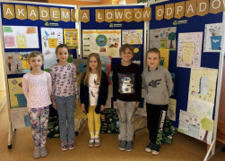 Uczniowie stoją przed ścianką, na której znajdują się prace plastyczne 