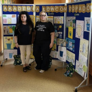 Dwie kobiety stoją przed ścianką, na której znajdują się prace plastyczne 