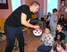 Grupa dzieci i mężczyzna. Mężczyzna pokazuje dzieciom sprzęt wykorzystywany w wspinaczce górskiej 
