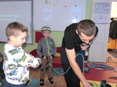 Mężczyzna i dwaj chłopcy. Mężczyzna prezentuje dzieciom sprzęt wykorzystywany do wspinaczki górskiej 