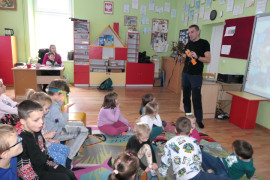 Mężczyzna i grupa dzieci. Mężczyzna prezentuje dzieciom sprzęt przeznaczony do wspinaczki górskiej 