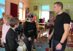 Mężczyzna prezentuje dzieciom sprzęt przeznaczony do wspinaczki górskiej 