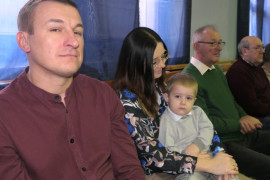 Osoby siedzą obok siebie. Na kolanach kobiety siedzi mały chłopiec 