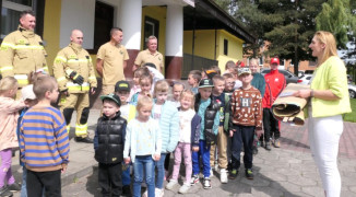 Strażacy i dzieci stoją przed budynkiem OSP