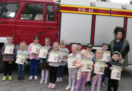 Dzieci i kobieta stoją obok samochodu strażackiego. Dzieci trzymają w dłoniach dyplomy
