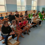 Grupa dzieci siedząca na drewnianych ławkach 