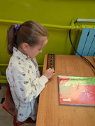 Dziewczynka siedzi przy szkolnej ławce. Dziewczynka rozwiązuje zadania z matematyki 