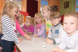 Dzieci stoją przy stoliku, na którym znajdują się szklanki z wodą 