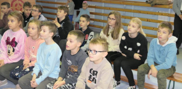 Grupa dzieci siedząca obok siebie na długiej ławce
