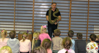 Sala gimnastyczna w szkole. Mężczyzna opowiada dzieciom o wężach. Prezentuje je też uczniom 