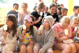 Dzieci siedzą obok siebie i jedzą lody