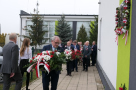 Mężczyzna składa kwiaty pod tablicą pamiątkową 