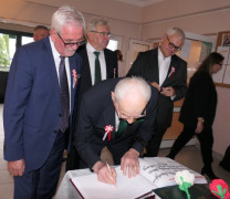 Mężczyźni stoją obok siebie. Jeden z nich wpisuje się do pamiątkowej księgi