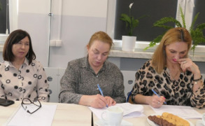 Trzy kobiety siedzą obok siebie przy stole. Kobiety trzymają w ręku długopisy 