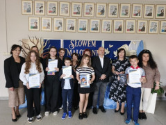 Grupa osób: dorośli i dzieci stoją obok siebie. Dzieci trzymają w dłoniach dyplomy 