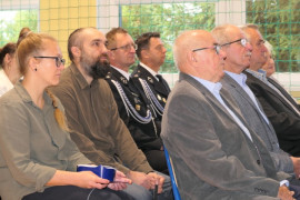 Grupa osób siedząca na krzesłach. Uczestnicy akademii szkolnej 