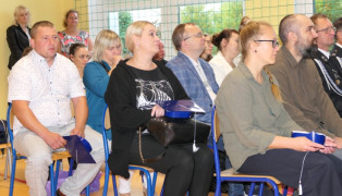 Grupa osób siedząca na krzesłach obok siebie. Uczestnicy akademii szkolnej 