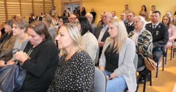 Grupa osób siedząca na krzesłach obok siebie. Uczestnicy akademii szkolnej 