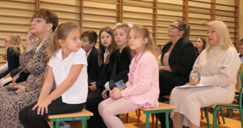 Grupa osób siedzi obok siebie. Osoby siedzą na ławce
