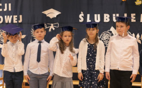 Grupa dzieci w odświętnych strojach. Dzieci mają na głowach granatowe birety 