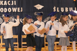 Grupa uczniów w galowych strojach. Uczniowie na głowach mają granatowe birety
