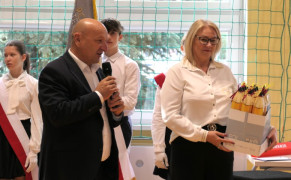 Kobieta i mężczyzna. Mężczyzna trzyma w ręku mikrofon, a kobieta prezenty dla pierwszoklasistów 
