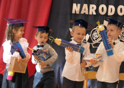 Grupa zadowoli=onych dzieci. Dzieciaki na głowach mają granatowe birety, a w ręku trzymają prezenty 
