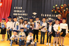 Grupa uczniów stojących obok siebie. Wszyscy mają na głowach granatowe birety 