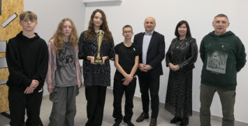 Grupa osób: dorośli i dzieci. Dziewczyna trzyma w ręku puchar