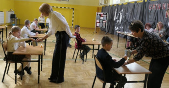 Dzieci siedzą w ławkach. Trwają przygotowania do szkolnego konkursu