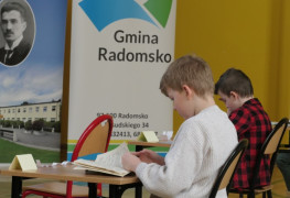 Dwaj chłopcy siedzą w ławkach i czytają fragmenty książek 