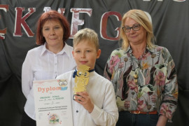 Chłopiec prezentuje otrzymaną statuetkę. Obok chłopca stoją dwie kobiety