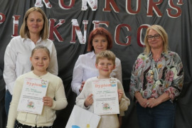 Dziewczynka i chłopiec prezentują dyplomy. Za dziećmi stoją trzy kobiety