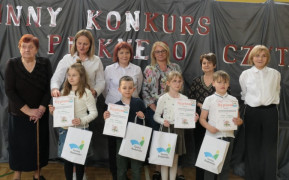 Dzieci trzymają w rękach zdobyte dyplomy. Za dziećmi stoją kobiety