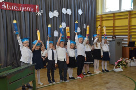 Grupa uczniów w niebieskich biretach na głowie 